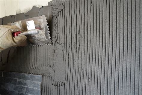 ranka klijuoja plytelę prie sienos